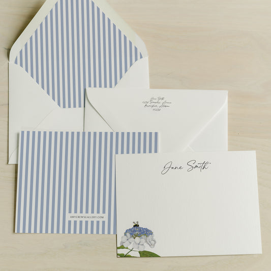 Stationery set with striped blue and white card, envelope, and letterhead on a beige background. Art by Amy Crews Gallery